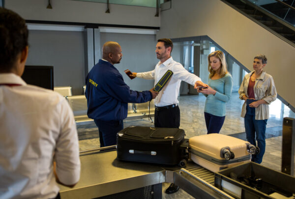 Security guard frisk passengers standing in queue at airport terminal