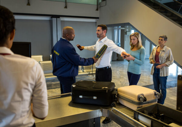 Security guard frisk passengers standing in queue at airport terminal